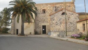 A stone building with a palm tree in front, a bench, and a street. - Sardinia International House (Zeddiani)