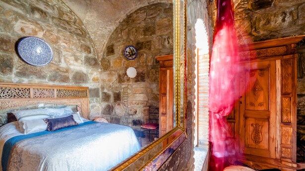 A stone-walled bedroom with a bed, a wooden cabinet, and a decorative plate on the wall. - El Asturiano (Tarifa)