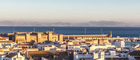 Un paisaje urbano costero con arquitectura histórica, incluyendo un castillo destacado y murallas fortificadas.