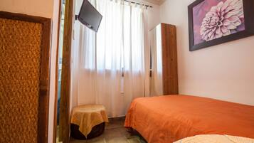 Un dormitori amb un llit, una televisió penjada a la paret, una finestra amb cortines i un quadre.