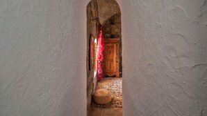 A narrow hallway with a wooden door at the end, a small round seating area, and a red curtain. - El Asturiano (Tarifa)