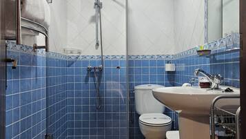 Een badkamer met blauwe tegels, een douchecabine van glas, een toilet en een wastafel.