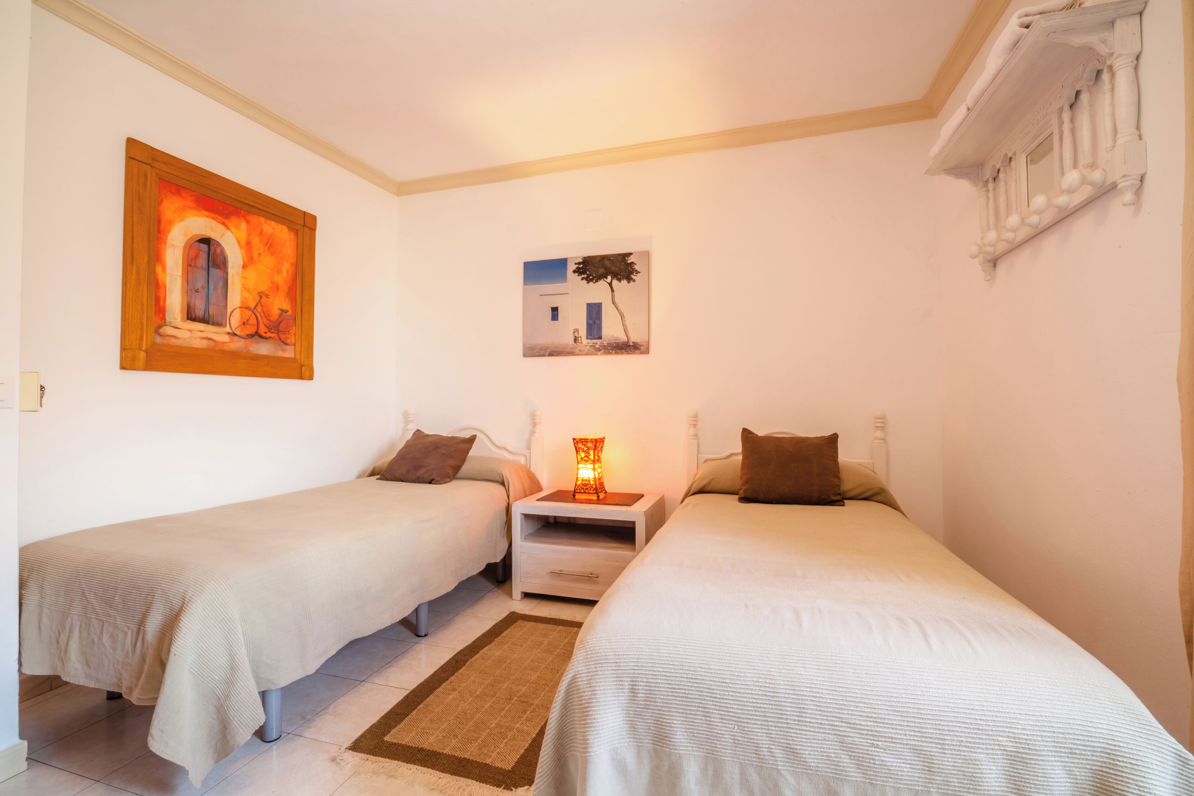 Une chambre avec deux lits simples, une table de chevet avec une lampe et deux tableaux au mur.