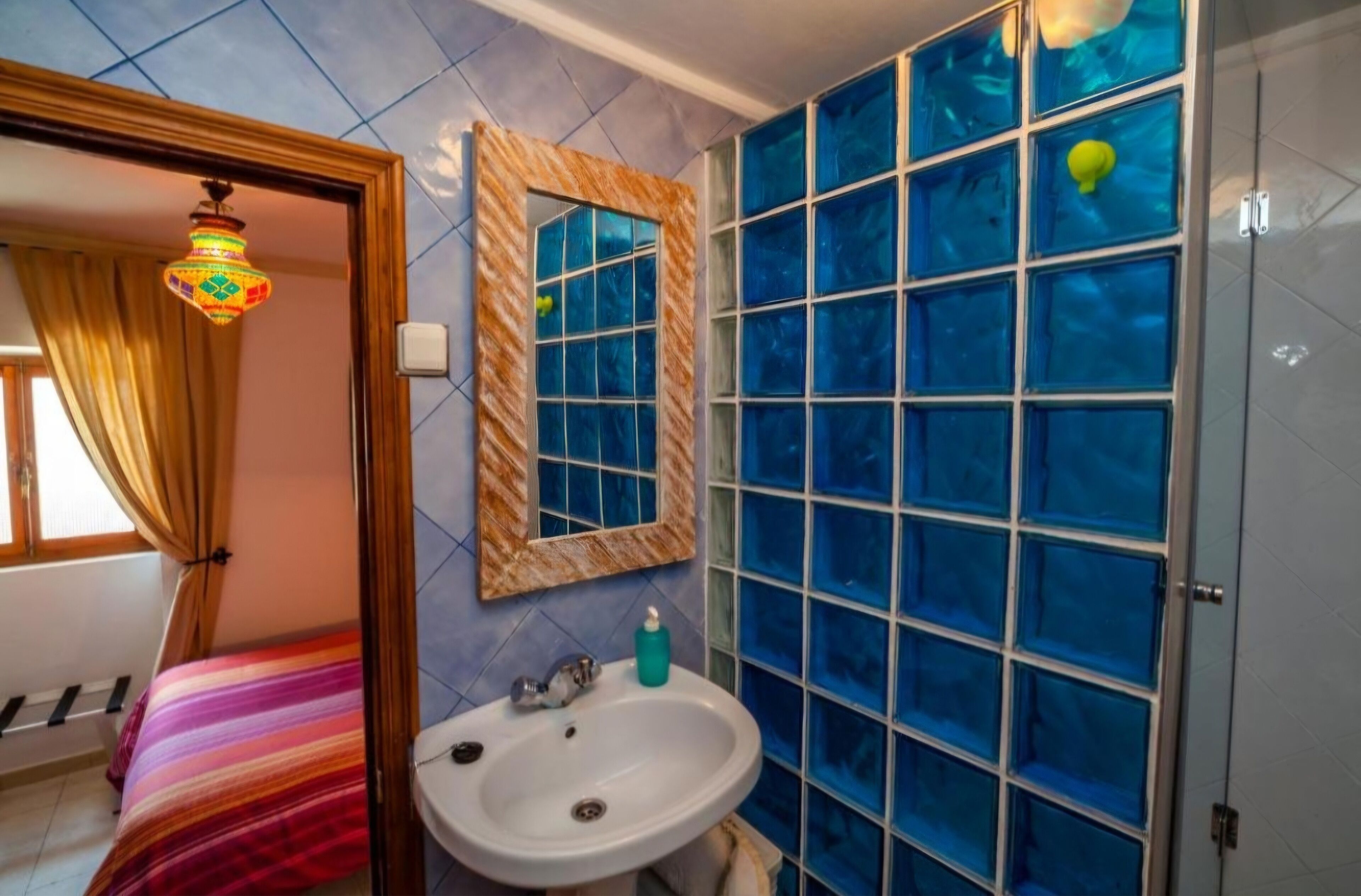 A bathroom with a sink, mirror, and blue-tiled shower enclosure.