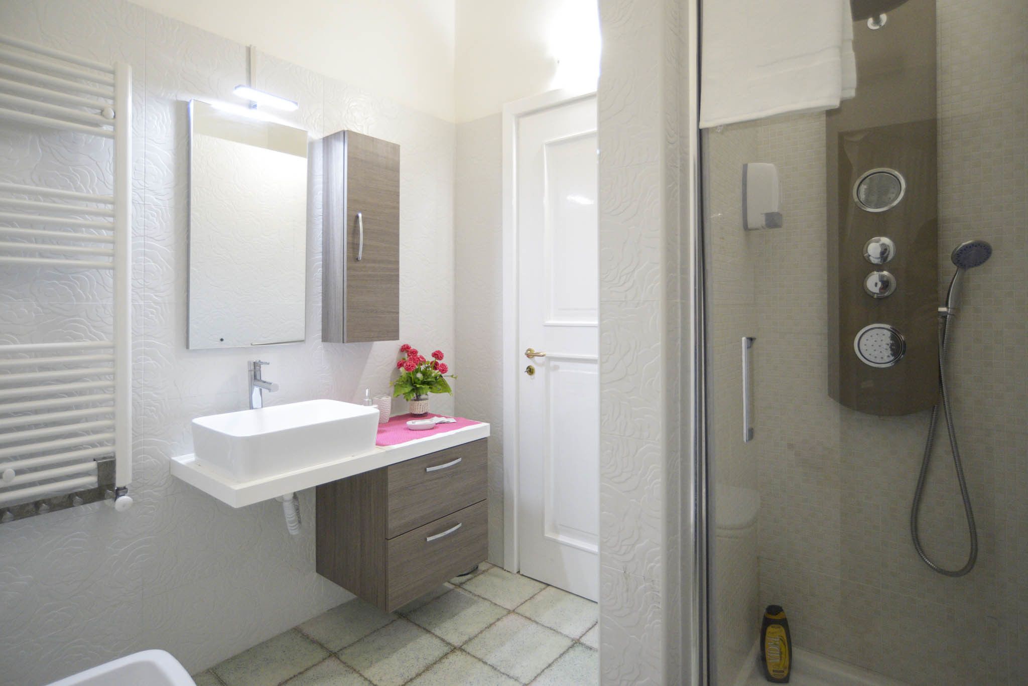 A bathroom with a white sink, a mirror, a shower with controls, and a door.