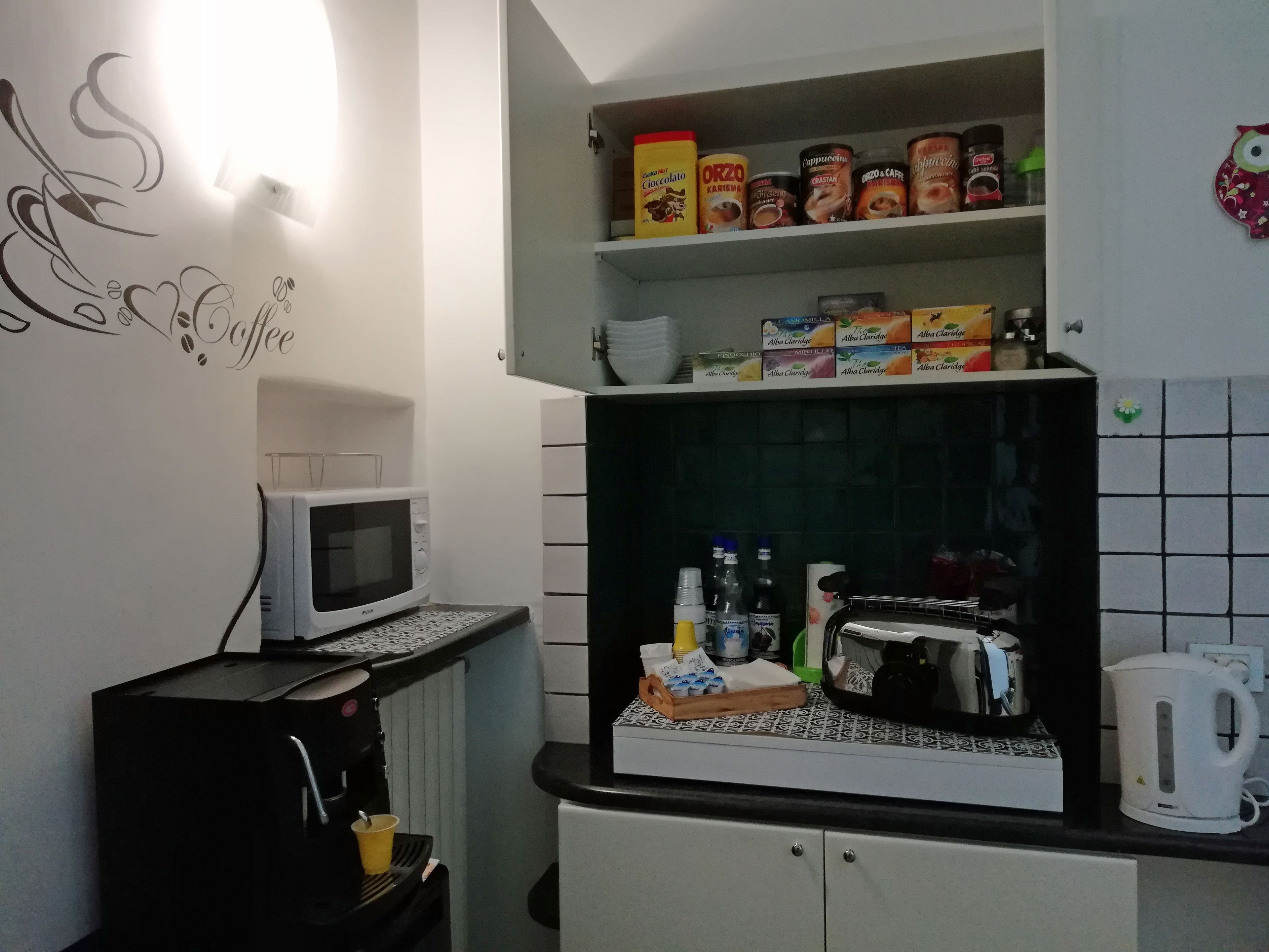 Une cuisine équipée d’un four à micro-ondes, d’une machine à café et de différentes sortes de café disposées sur des étagères.