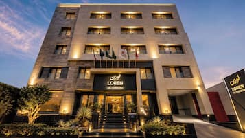 Een modern hotelgebouw met meerdere verdiepingen, een opvallende entree met treden en vlaggen buiten.