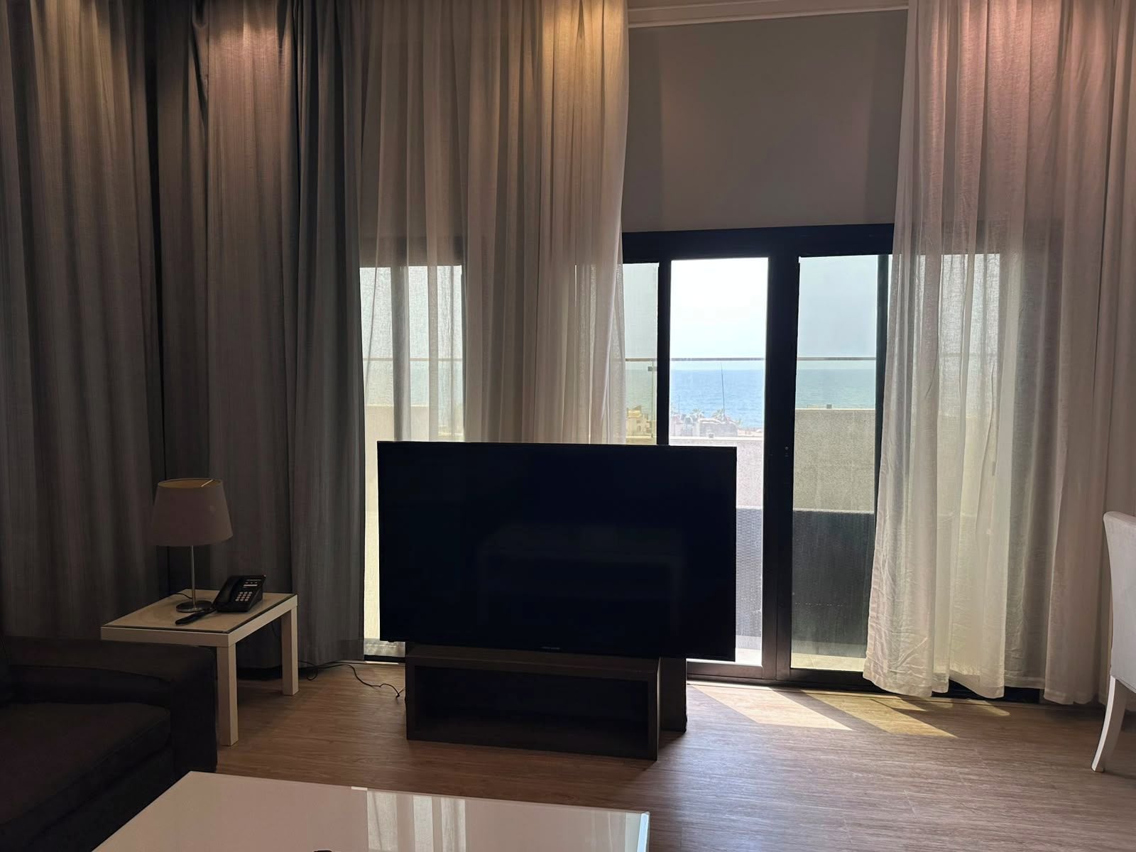 A living room with a flat-screen TV, a small table with a lamp, and a sofa.