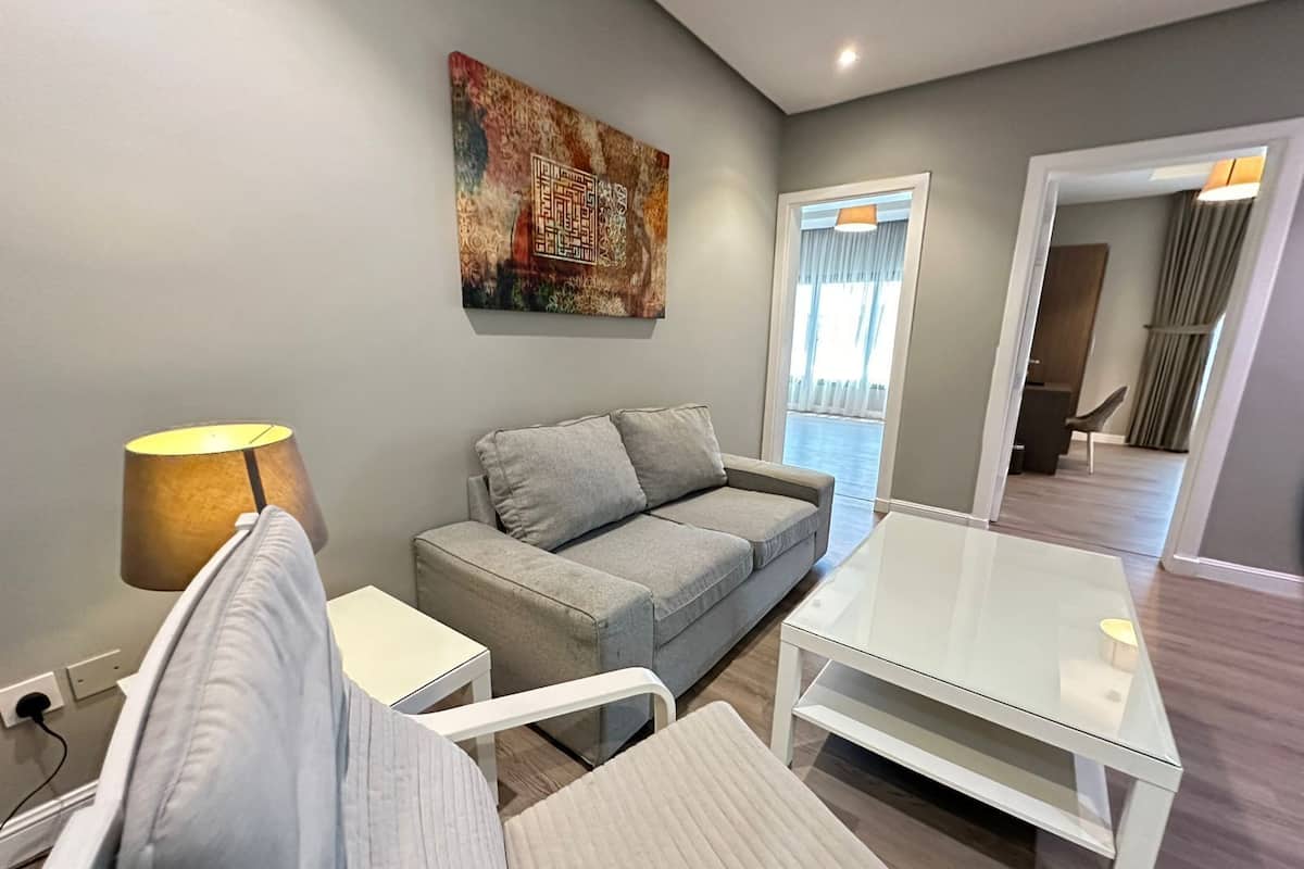 A modern living room with a grey sofa, a glass coffee table, and a lamp.