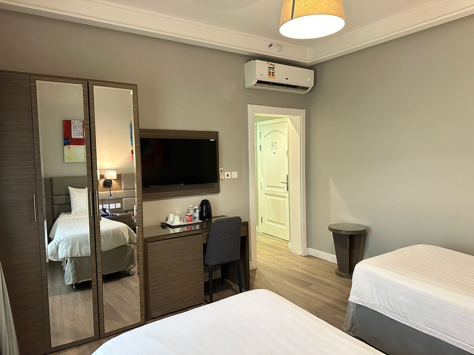 A hotel room with a bed, a desk with a chair, a television, and an air conditioning unit.
