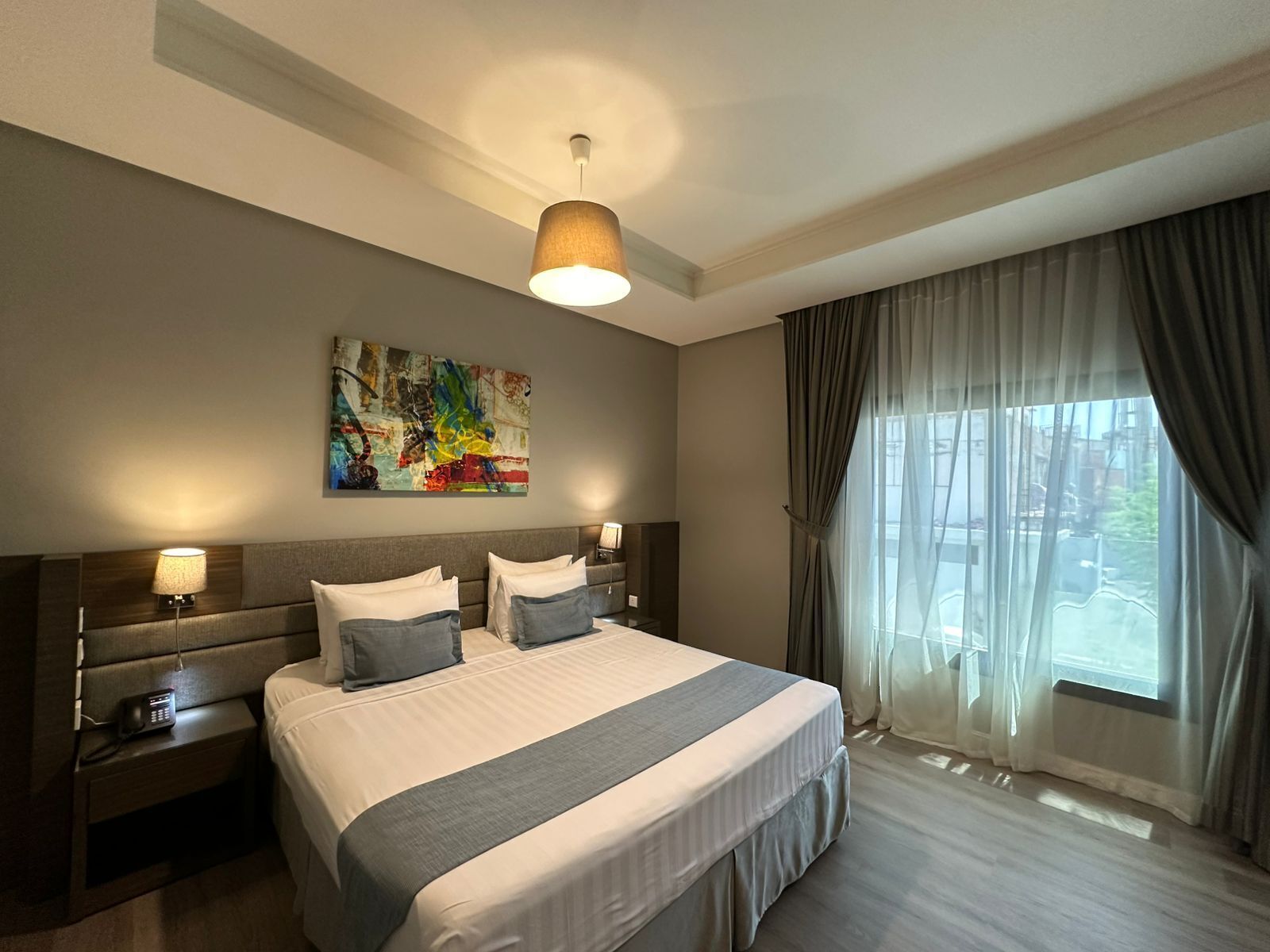 Une chambre d’hôtel avec un grand lit, deux tables de chevet, un tableau au mur et une fenêtre avec des rideaux.