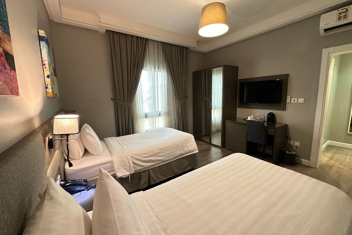 A hotel room with two beds, a desk, a TV, and a wardrobe.