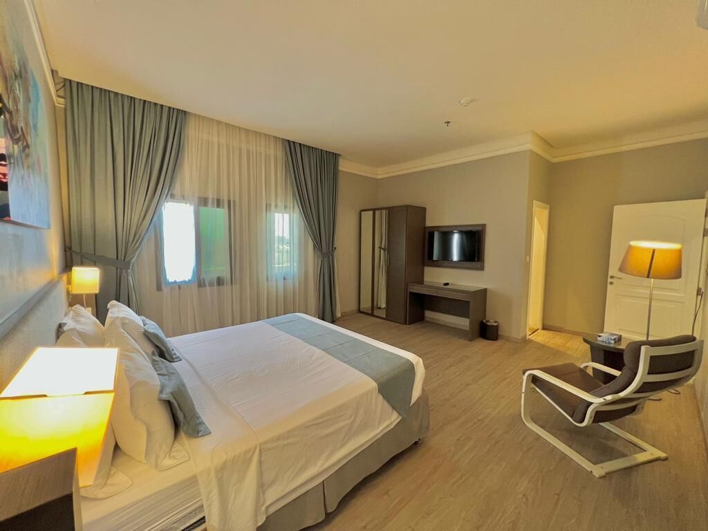 A hotel room with a bed, a desk, a TV, a chair, and a lamp.