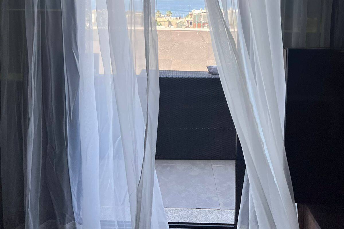 A room with sheer white curtains, a view of the beach, and a black mat at the entrance.