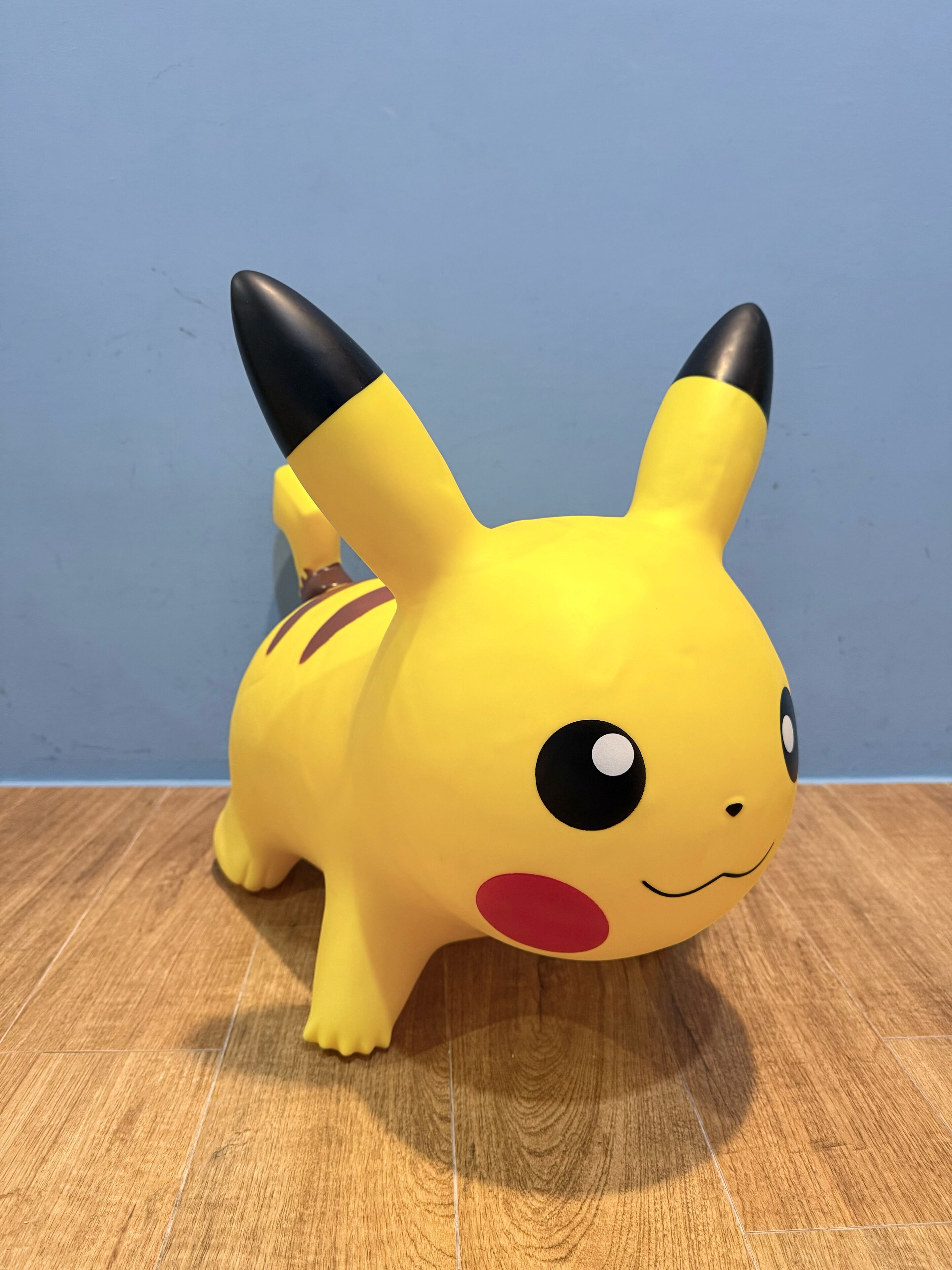 Een pluche Pikachu speeltje op een houten vloer, voor een blauwe muur.