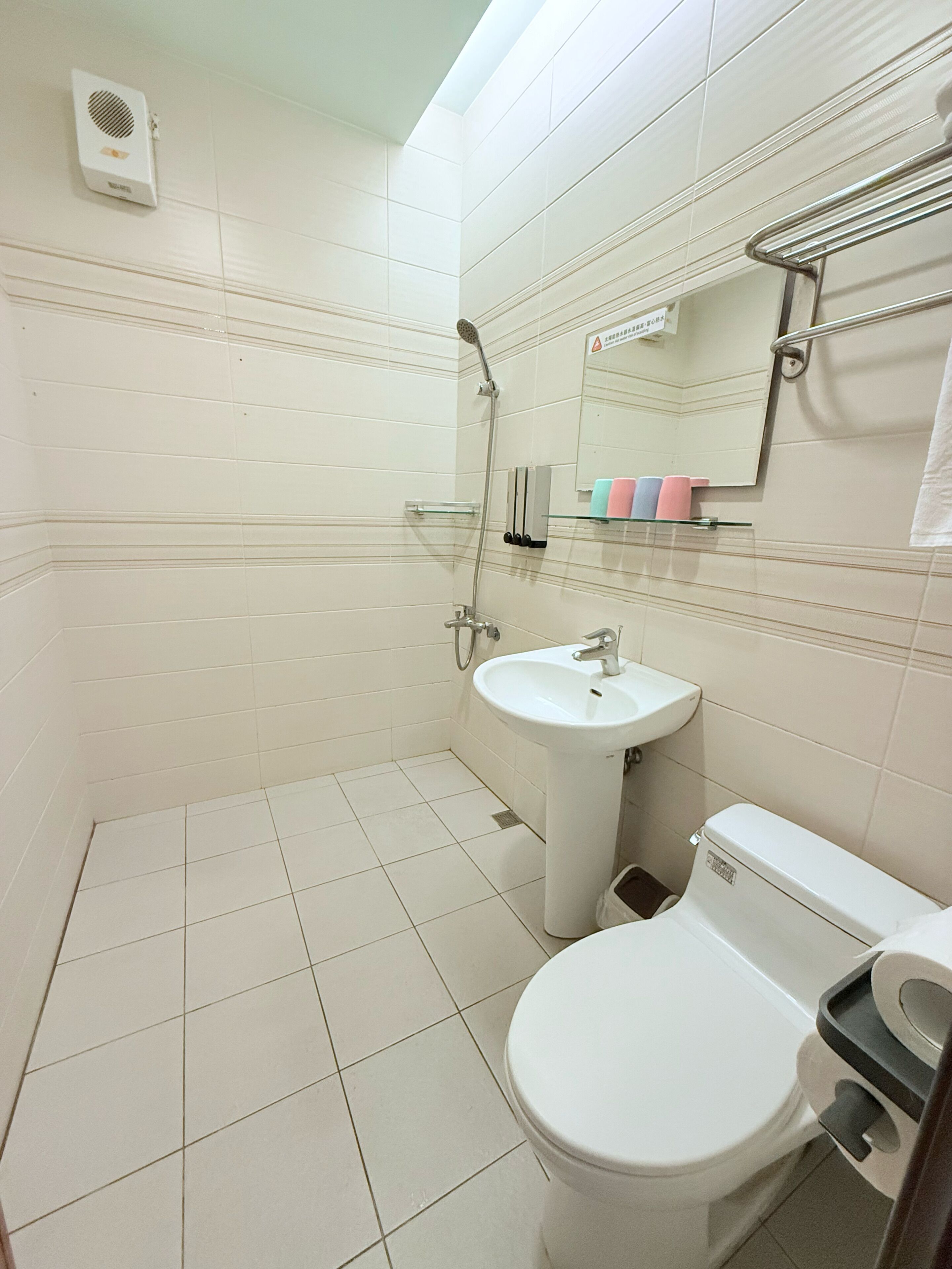 A bathroom with a toilet, sink, shower, and a mirror.