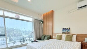 Une chambre d’hôtel avec un grand lit, une tête de lit en bois, un tableau, une table de chevet et une vue sur l’extérieur grâce à une porte coulissante.