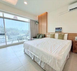 A hotel room with a large bed, a wooden headboard, a painting, a nightstand, and a view of the outdoors through a sliding door. - Lunatis Bay Hotel (Liuqiu)
