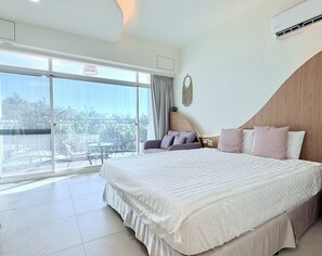 A hotel room with a large bed, a balcony with a table and chairs, and a view of the outdoors.