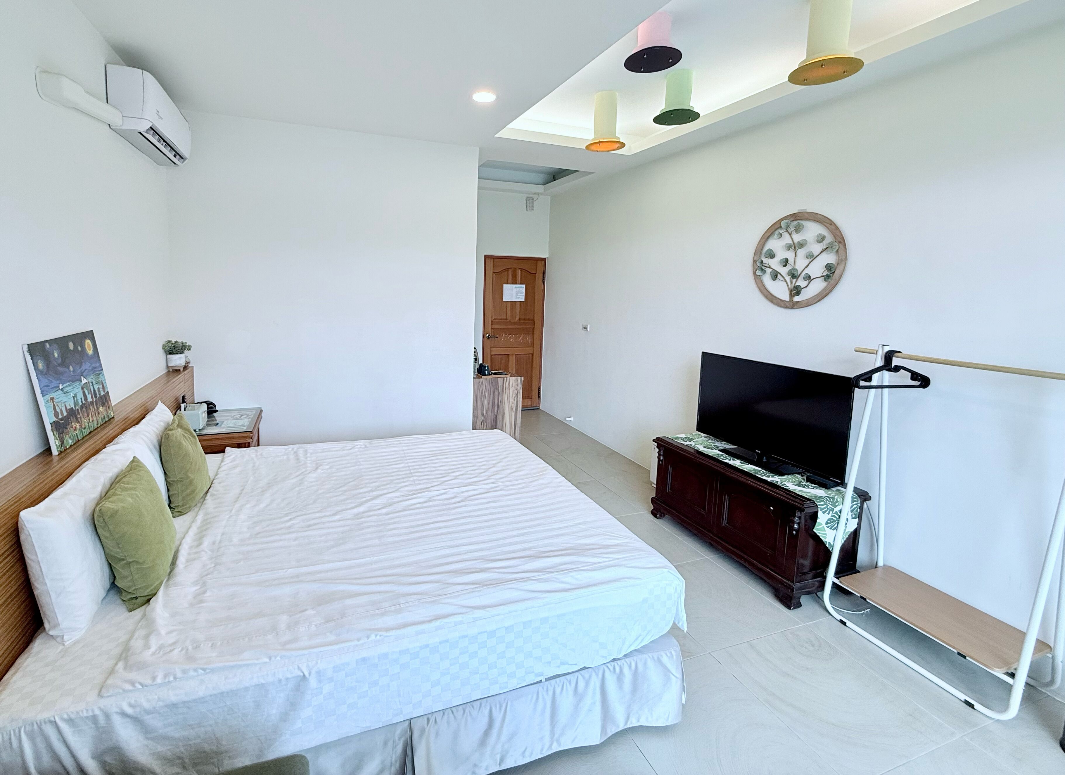 A bedroom with a bed, a TV, a painting, and a ceiling fan.