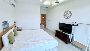 A bedroom with a bed, a TV, a painting, and a ceiling fan.