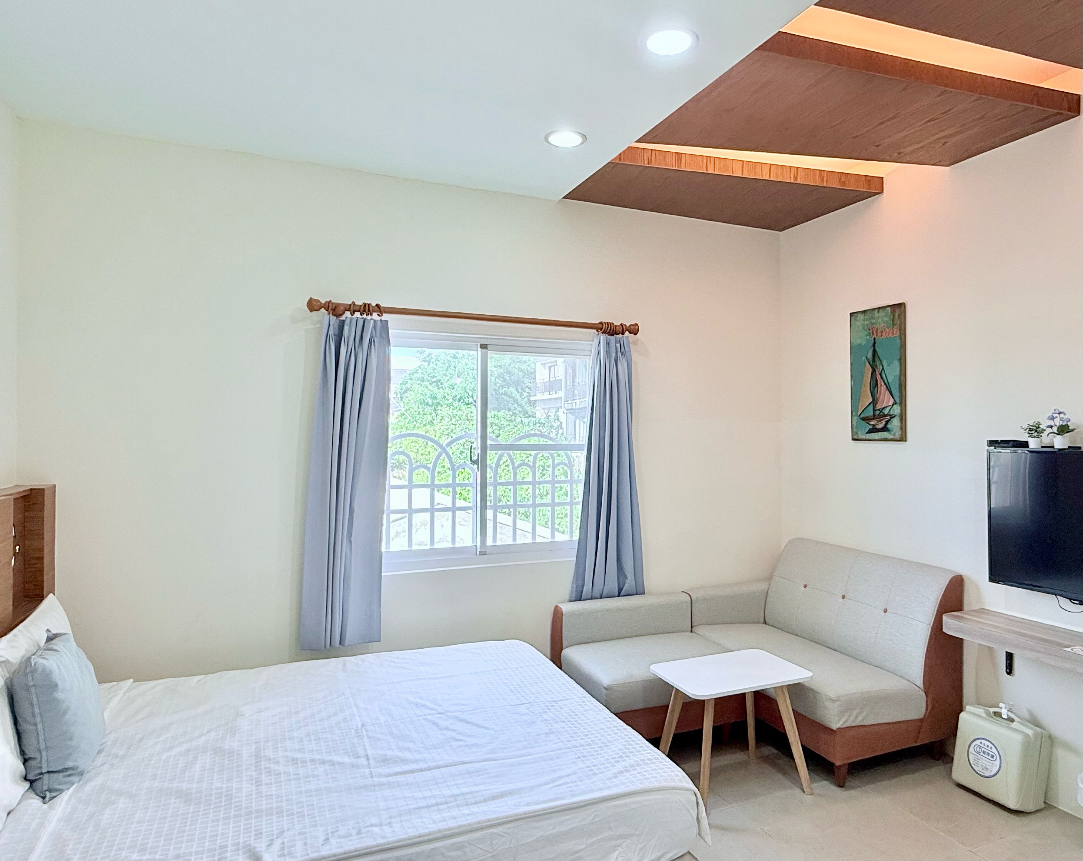 Un dormitorio con cama, sofá, una mesita, televisor y ventana con cortinas.
