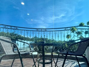 A balcony with wicker chairs and a table, overlooking a scenic view with trees and a clear sky.