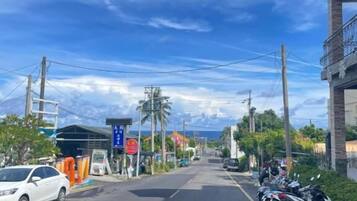 Eine Straße mit abgestellten Motorrädern und einem weißen Auto, mit Gebäuden an beiden Seiten und Stromleitungen darüber.