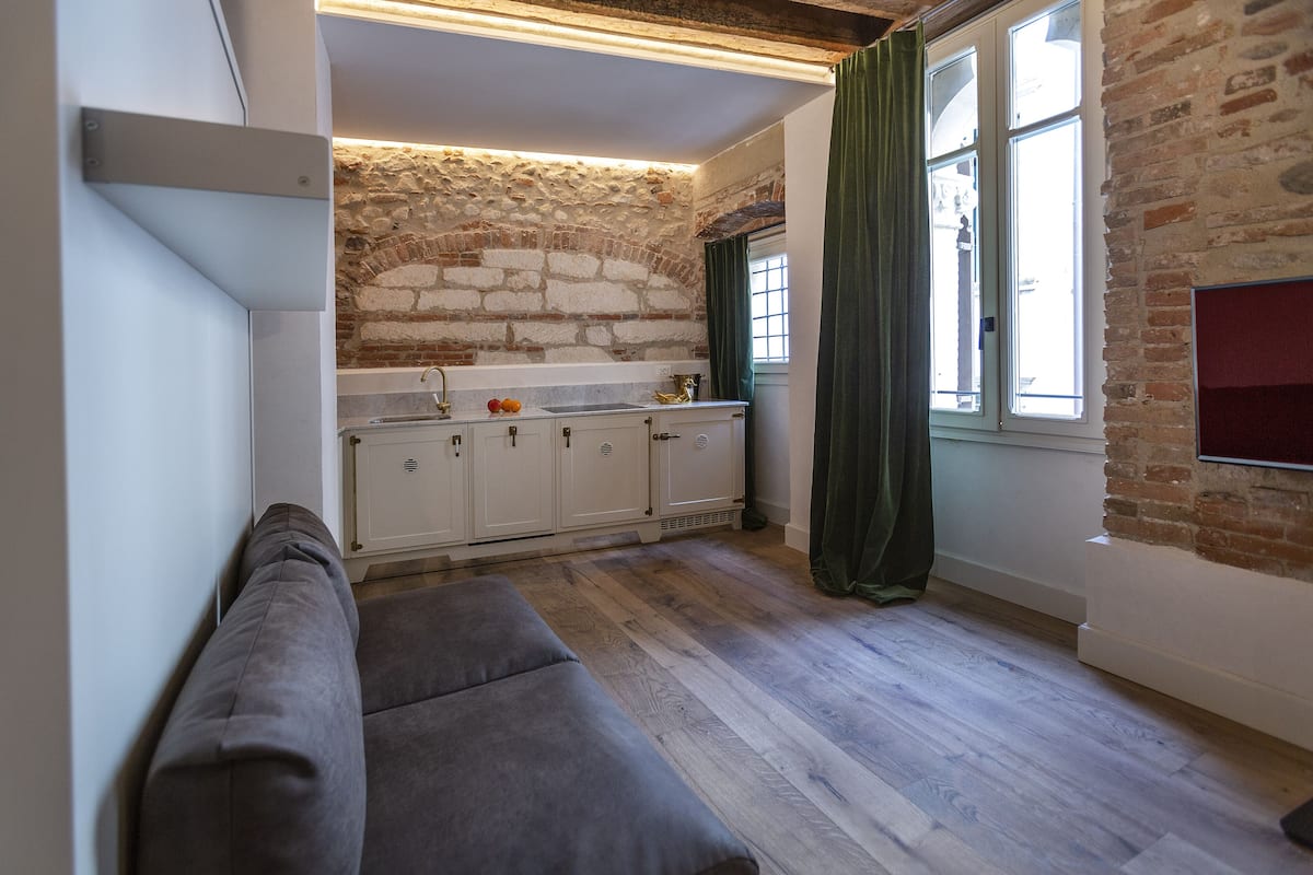 A compact kitchen with white cabinets, a stone wall, and a window with green curtains.