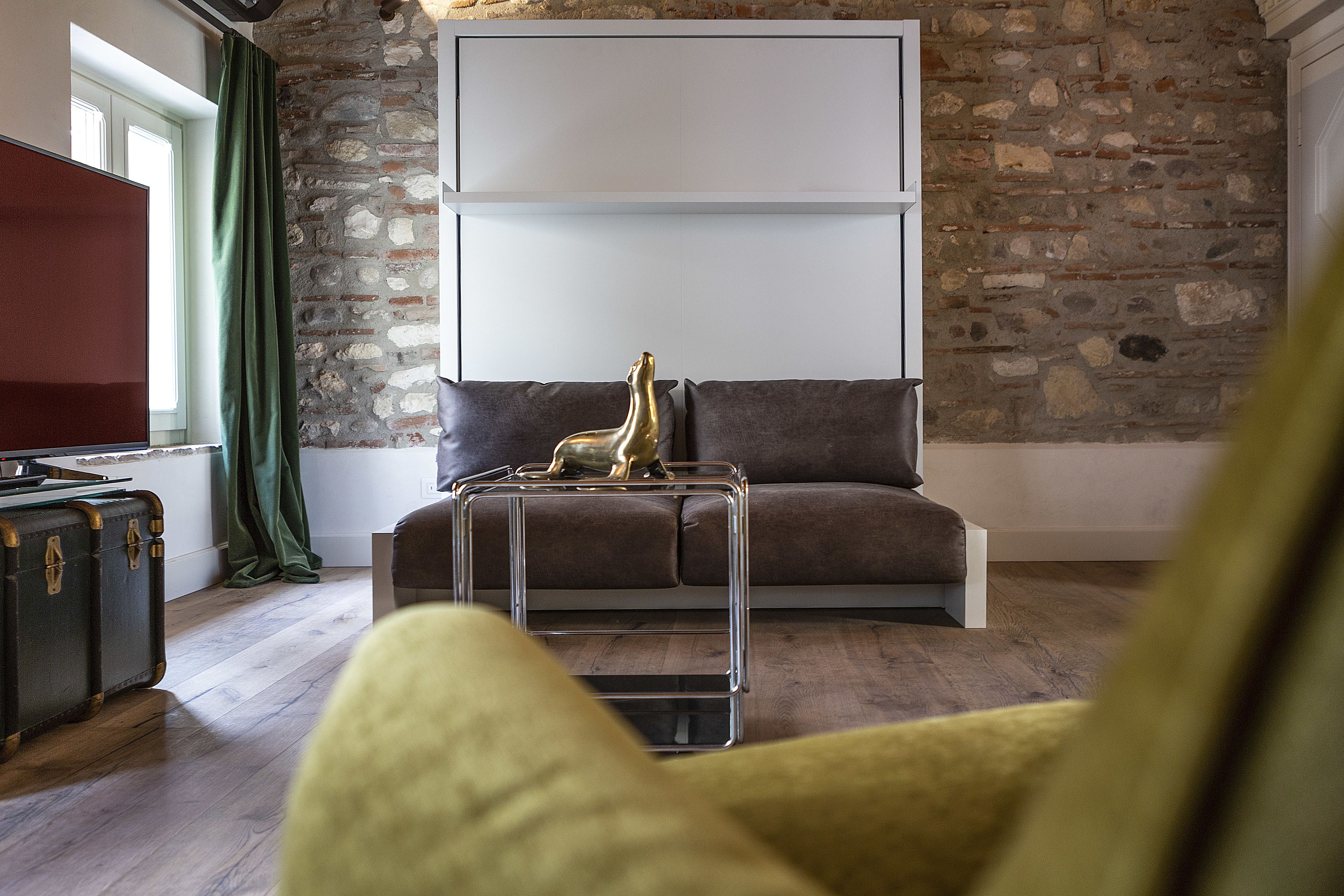 A living room with a stone wall, a brown sofa, a glass coffee table with a golden statue, and a television on the left.