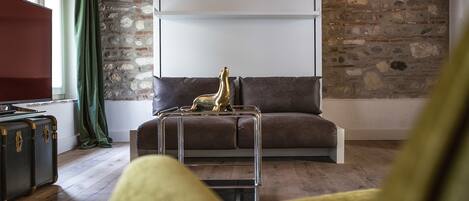 A living room with a stone wall, a brown sofa, a glass coffee table with a golden statue, and a television on the left.
