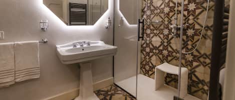 Un baño con un lavamanos pedestal, un espejo, una ducha con puerta de cristal y baldosas estampadas en el suelo y las paredes.