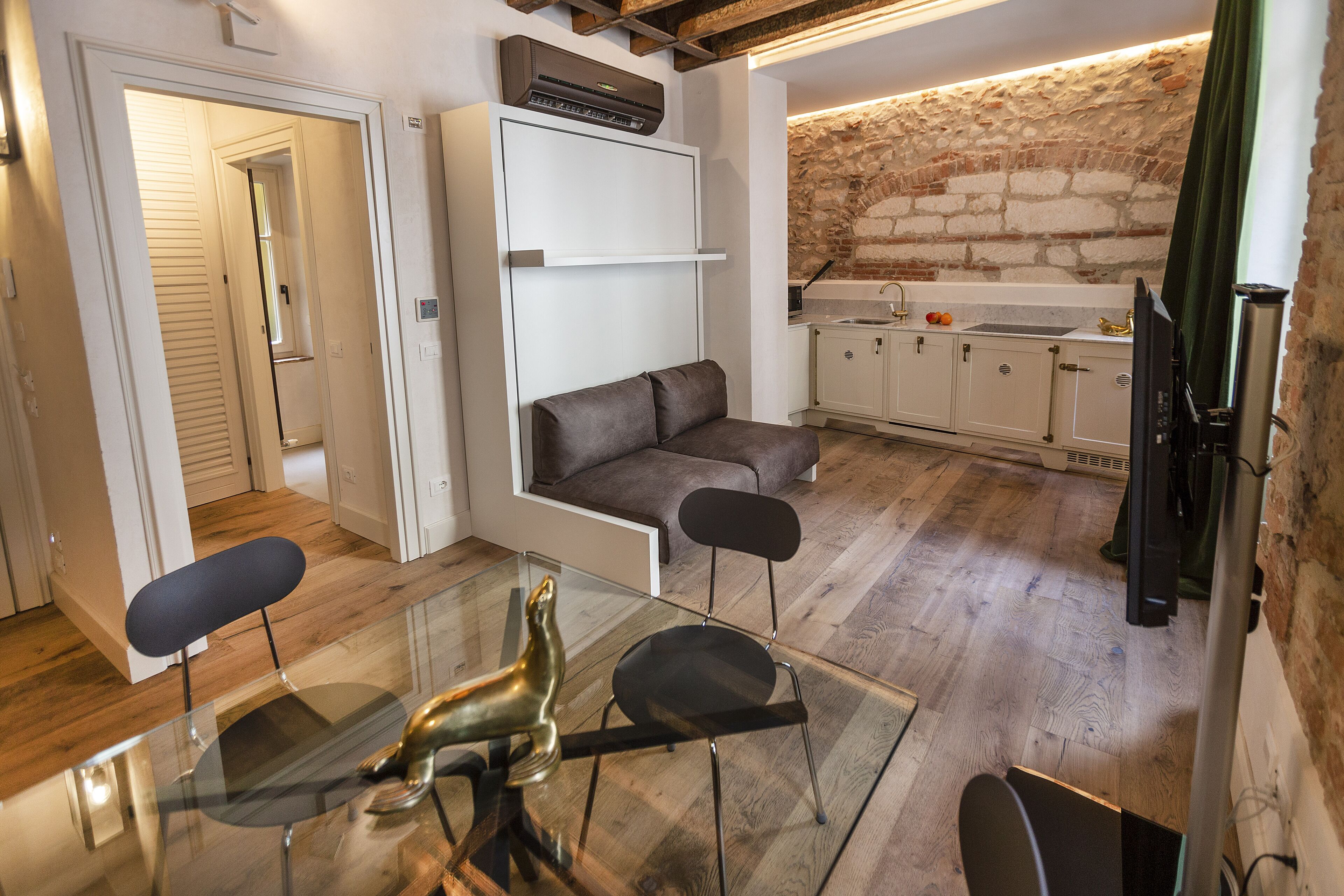 A compact kitchen with a brick wall, a sofa, and a glass dining table.