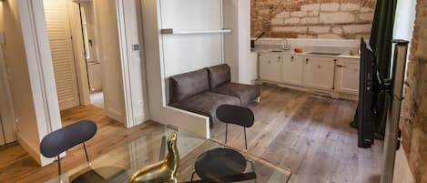Una cocina pequeña con pared de ladrillo, un sofá y una mesa de vidrio para comer.