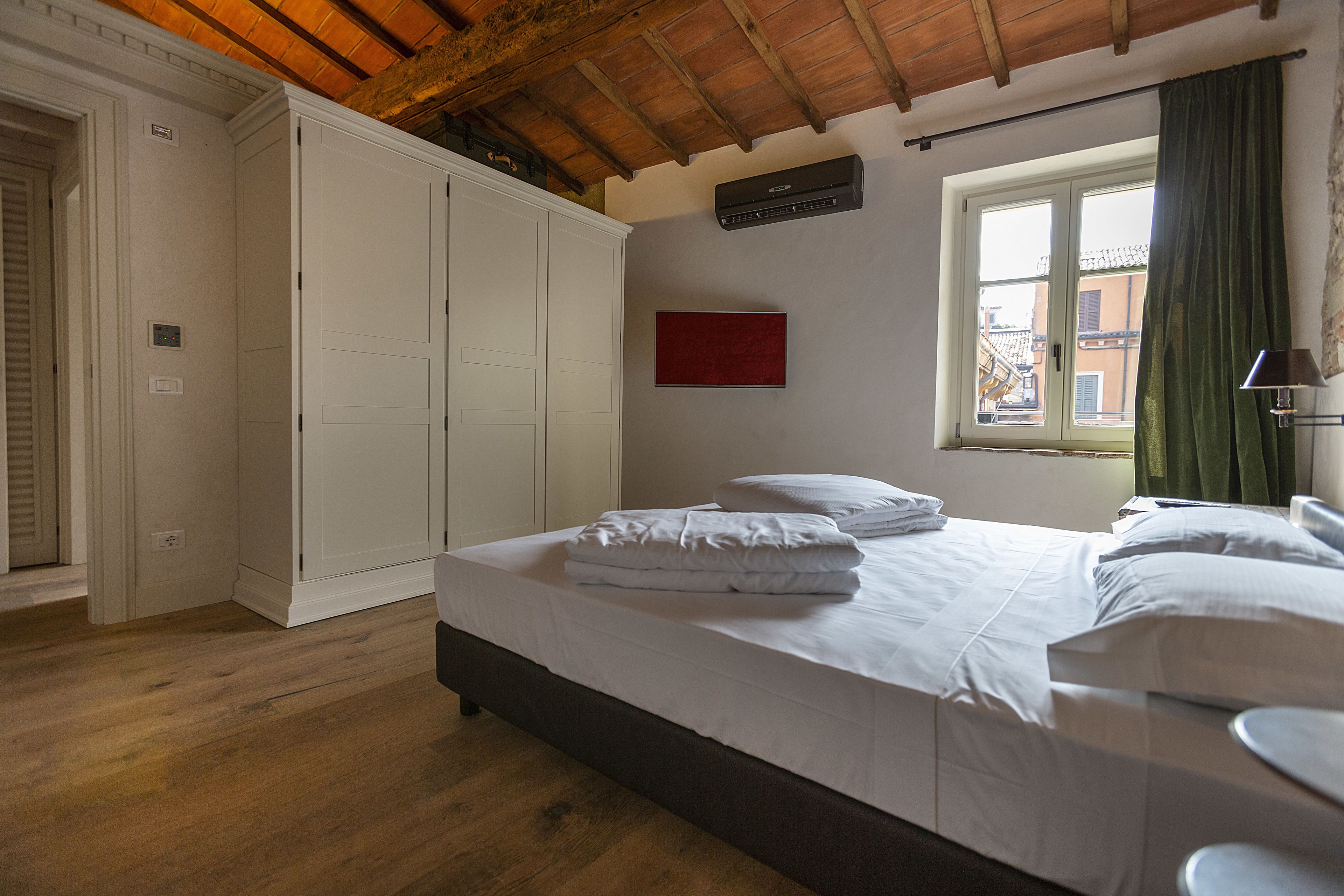A hotel room with a bed, a wardrobe, a window with curtains, and a red artwork on the wall.