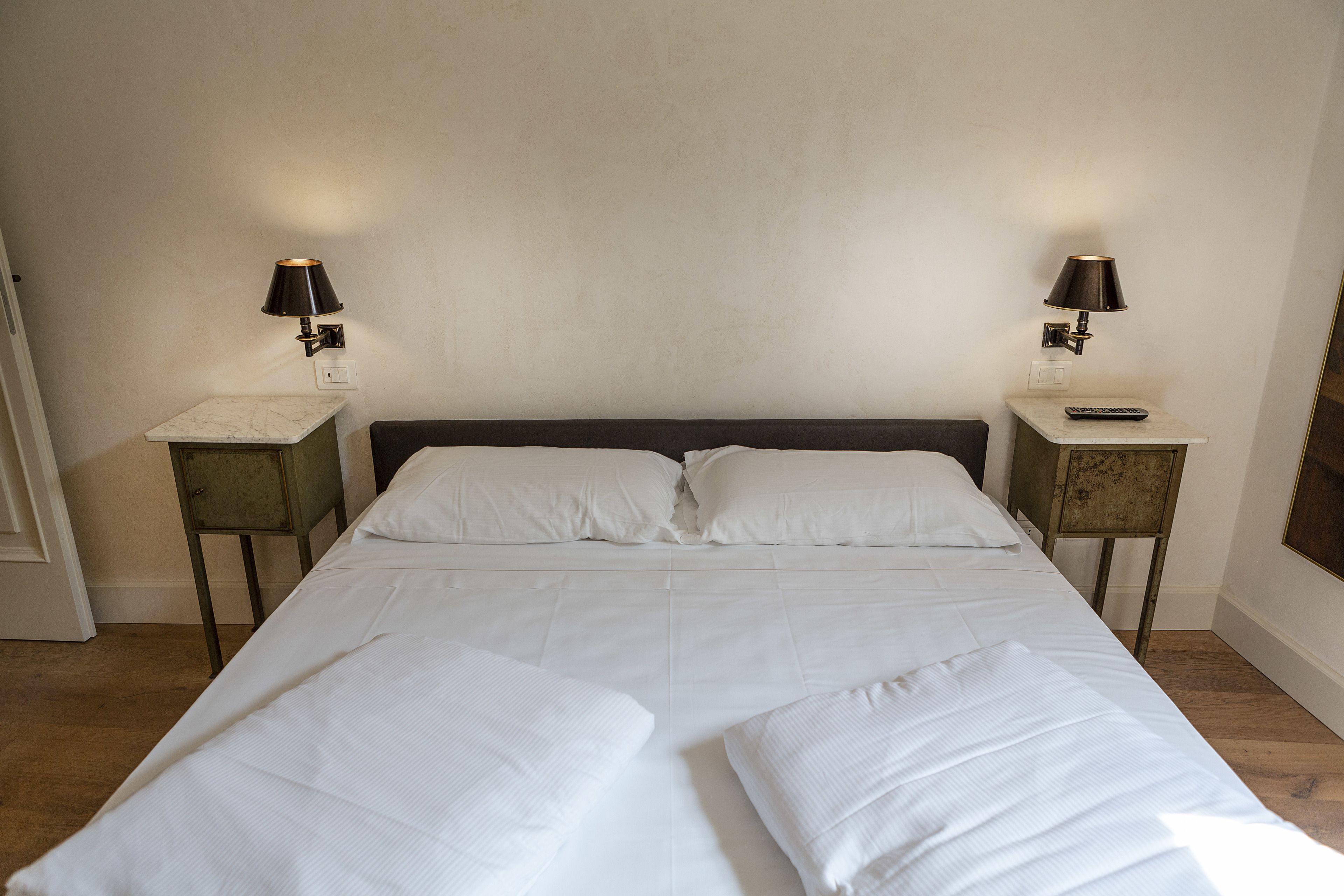 A double bed with white linens, two bedside tables with lamps, and a wooden floor.