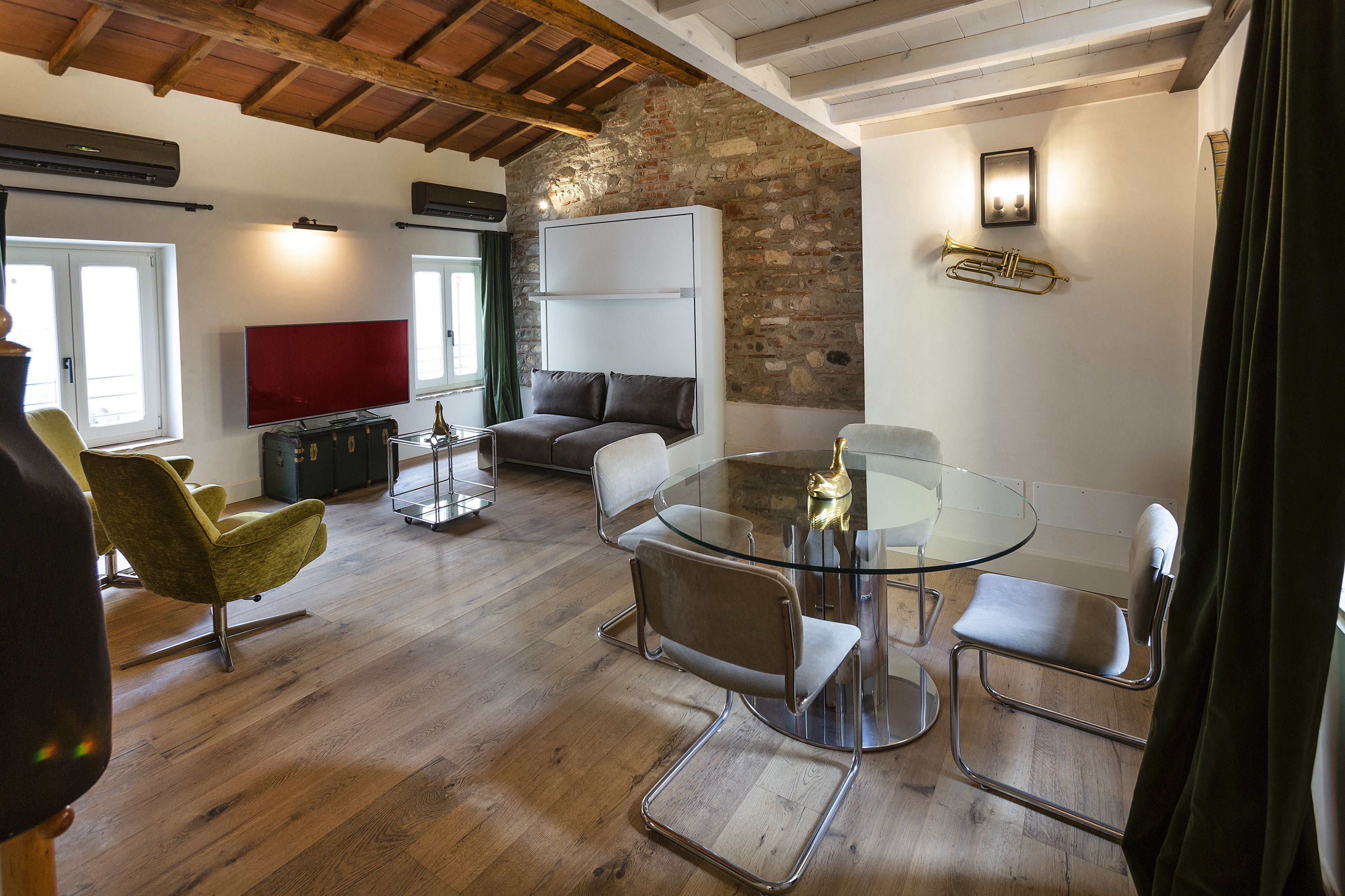 Una sala de estar moderna con una mesa de comedor de vidrio, asientos cómodos, un sofá y una pared de piedra.