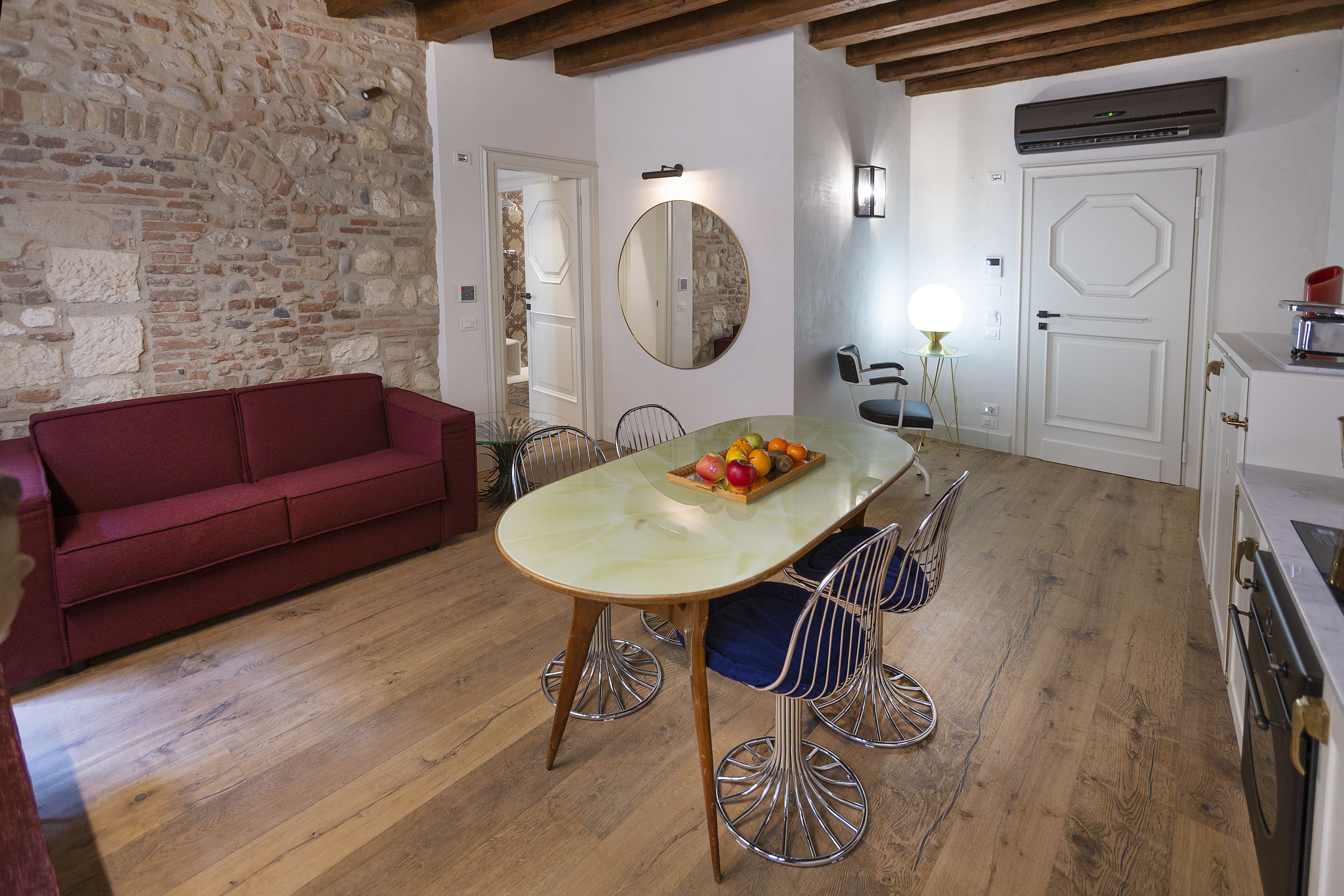 A dining area with a wooden table, chairs, a red sofa, and a stone wall.