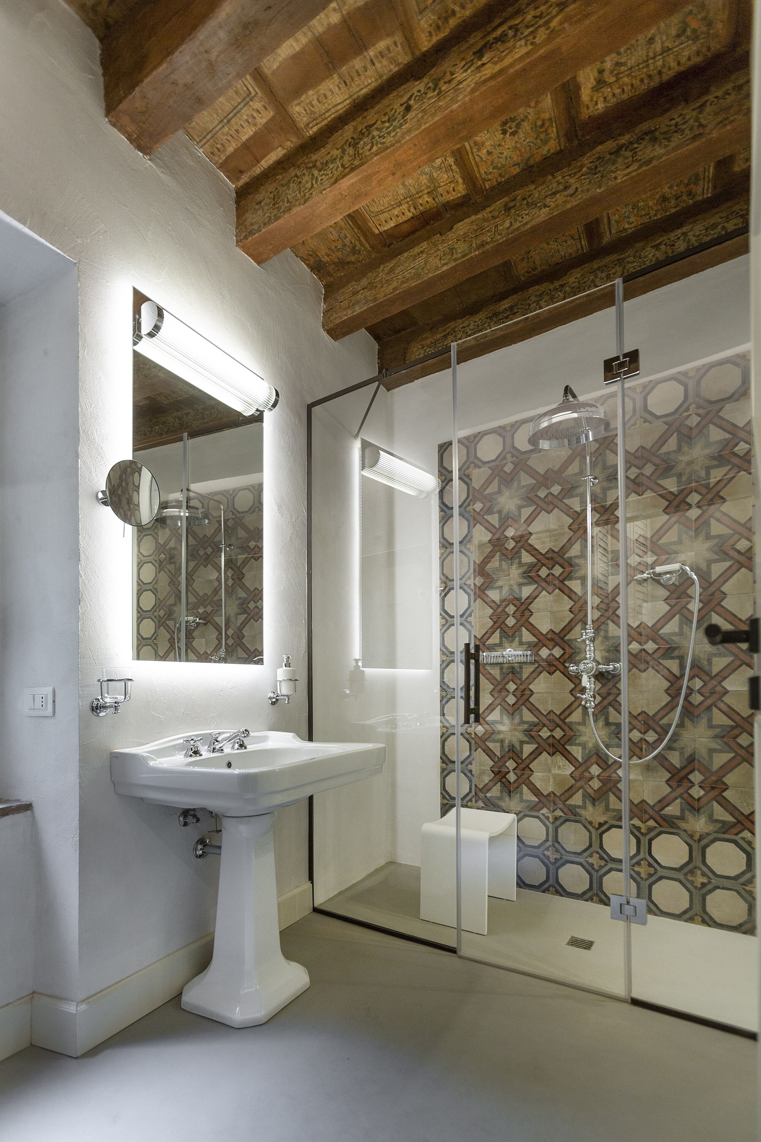 Un baño con lavamanos blanco, un espejo y una ducha con pared de azulejos estampados.