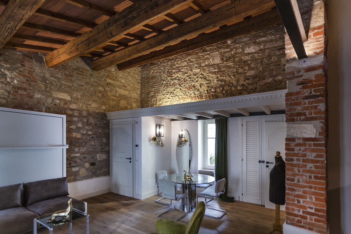 A room with exposed brick walls, a wooden ceiling, a round table with chairs, a sofa, and a mannequin.