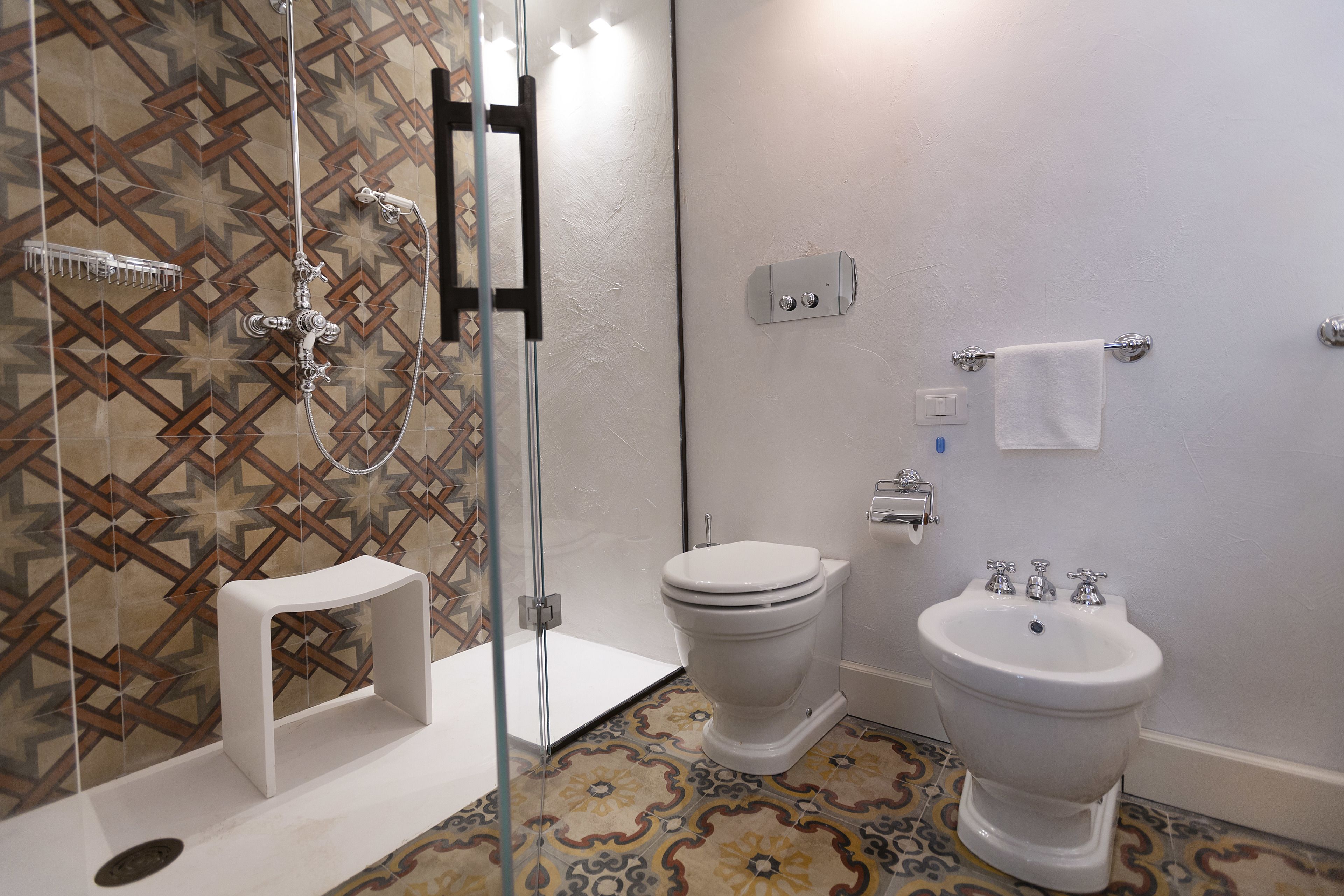 A bathroom with a shower, toilet, bidet, and a small white stool.