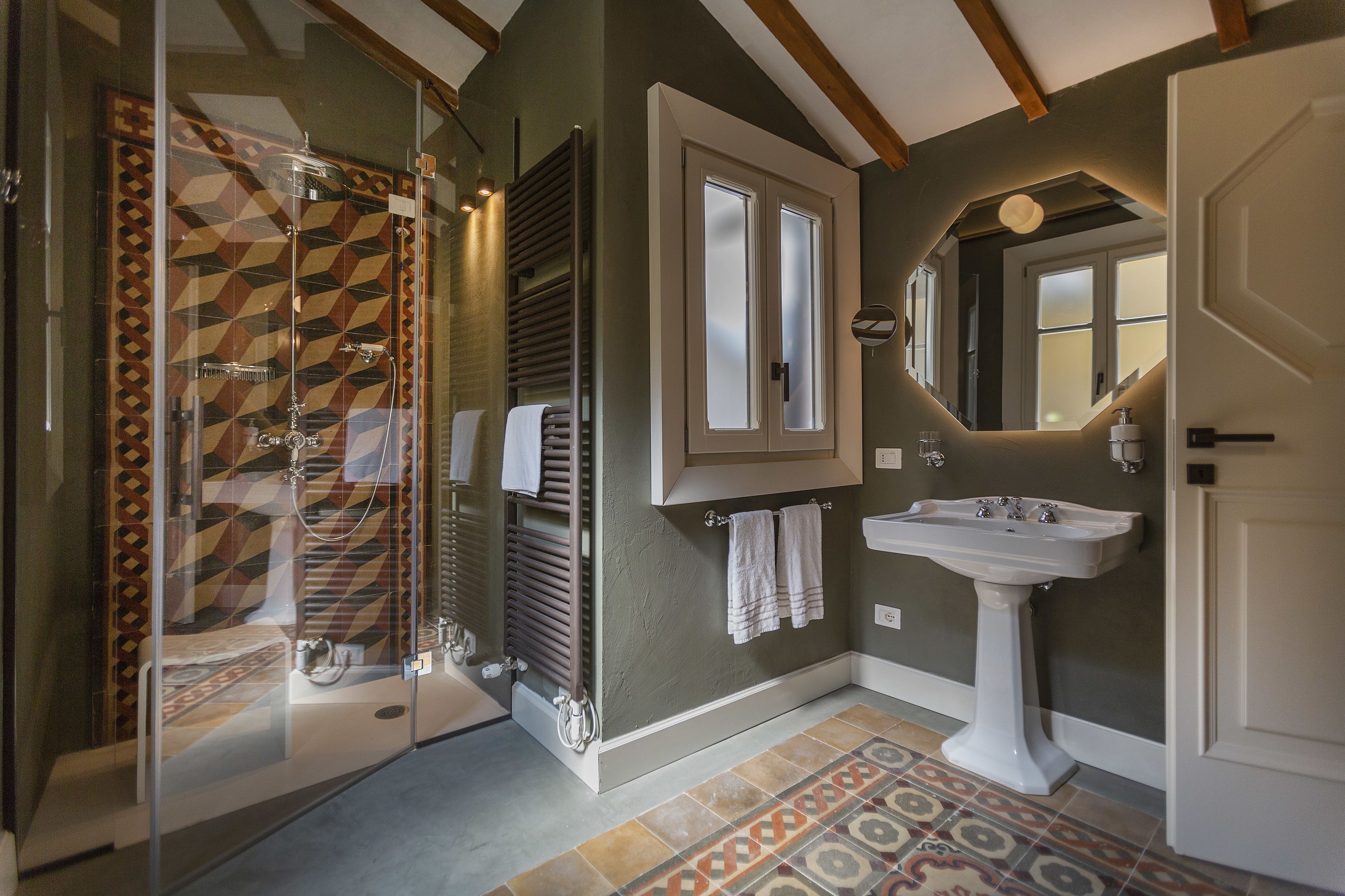 Une salle de bain avec une douche à parois de verre, un lavabo blanc et des carreaux à motifs.