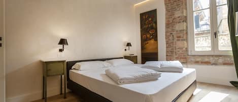 A neatly made bed in a room with a brick wall and a window.