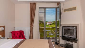 Habitación de hotel con cama, un sillón rojo, televisor y puerta corrediza de vidrio que da a un balcón con vista a una casa y follaje.