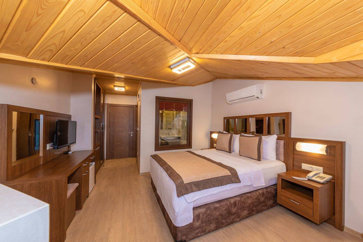 Une chambre avec un plafond en bois, un lit doté d’une tête de lit, une table de chevet avec une lampe et un téléviseur posé sur une commode en bois.