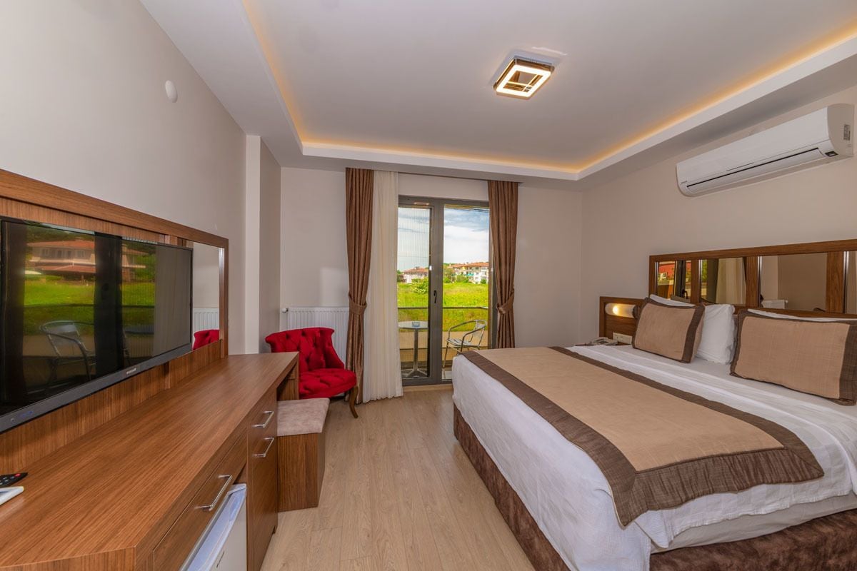 A modern hotel room with a large bed, a flat-screen TV, a wooden desk, and a balcony with a view.