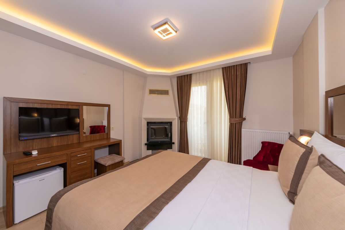 A hotel room with a large bed, a TV, a desk with a computer, and a small refrigerator.