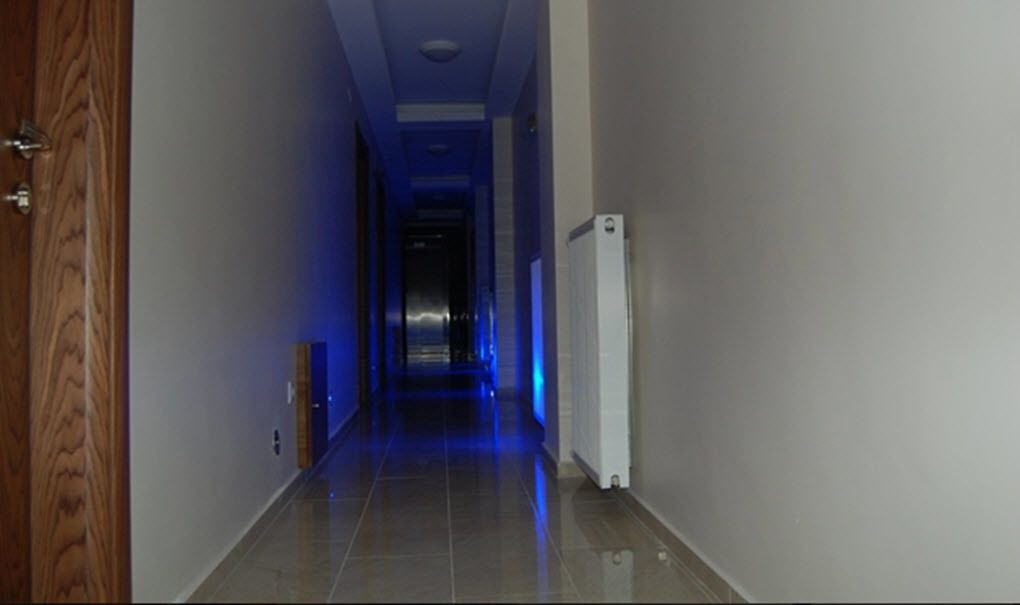 A narrow hallway with a wooden door on the left, a white radiator on the right, and a blue-lit corridor ahead.