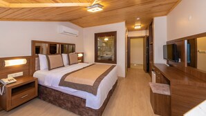 A hotel room with a wooden ceiling, a large bed with a headboard, a bedside table with a phone, a TV, and a wardrobe.