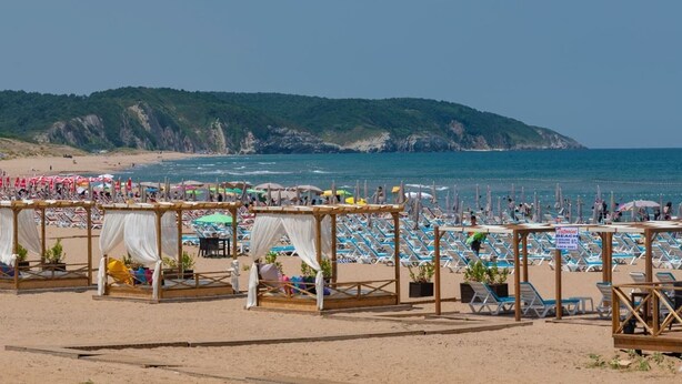 A beach with wooden cabanas, beach umbrellas, and lounge chairs.